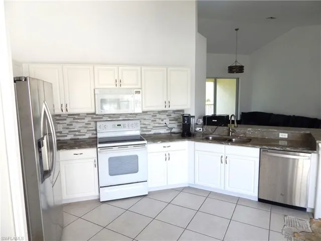 Kitchen with appliances with stainless steel finishes, white cabinetry, decorative light fixtures, and sink