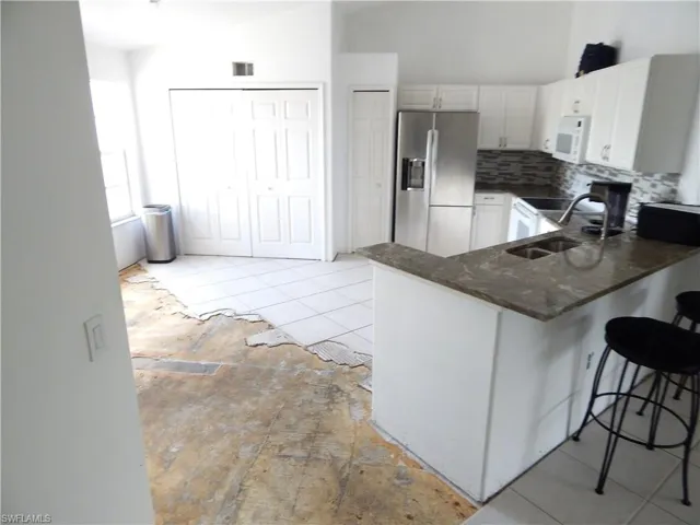 Kitchen with dark stone countertops, white cabinetry, white appliances, kitchen peninsula, and a breakfast bar area