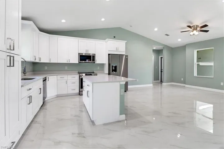 Kitchen with appliances with stainless steel finishes, vaulted ceiling, white cabinets, a center island, and ceiling fan