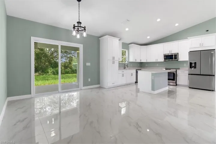 Kitchen with a chandelier, lofted ceiling, white cabinetry, stainless steel appliances, and decorative light fixtures
