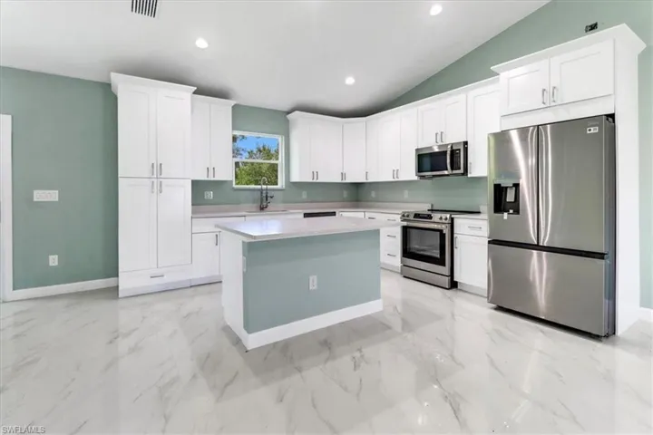 Kitchen featuring stainless steel appliances, vaulted ceiling, white cabinetry, and a kitchen island