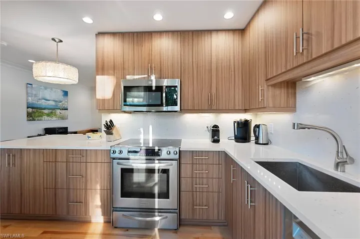 Kitchen with stainless steel appliances, light stone countertops, modern cabinets, pendant lighting, and a peninsula
