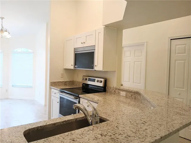 Kitchen with light stone counters, stainless steel appliances, white cabinetry, sink, and pendant lighting