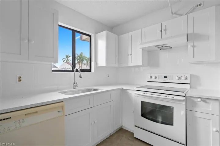 Kitchen with a textured ceiling, white cabinetry, sink, and white appliances
