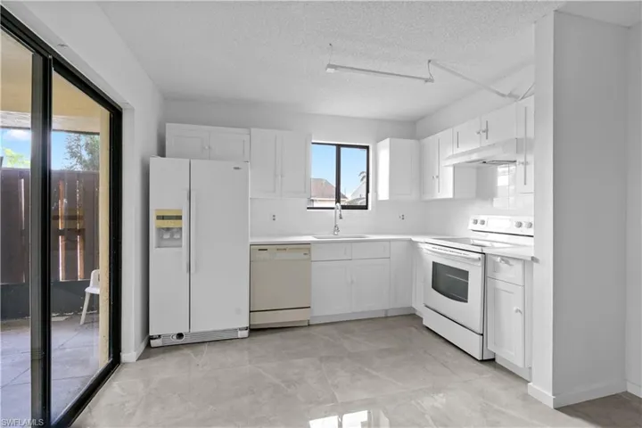 Kitchen featuring sink, backsplash, a textured ceiling, white appliances, and white cabinets