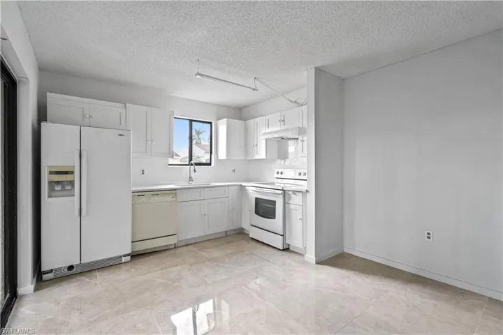 Kitchen with a textured ceiling, white cabinetry, sink, and white appliances