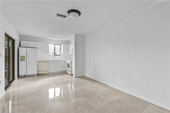 Kitchen with a textured ceiling, white appliances, white cabinetry, and sink