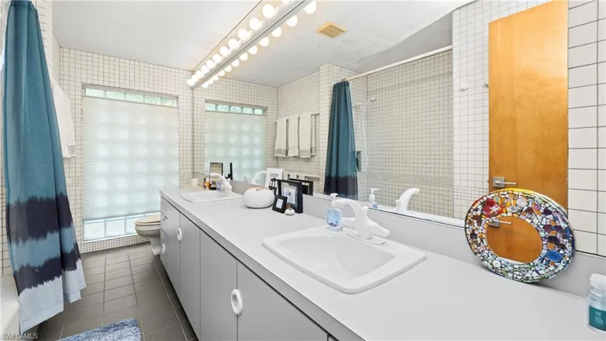 Full bath featuring double vanity, dark tile patterned floors, tiled shower, and tile walls