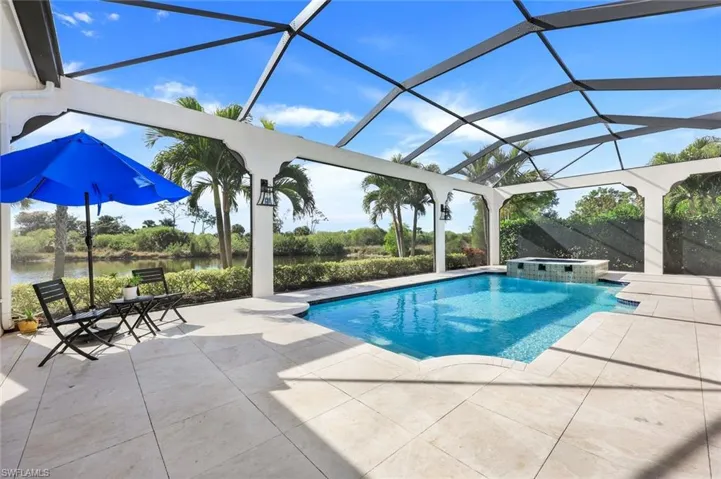 View of pool featuring a patio, a water view, a pool with connected hot tub, and glass enclosure