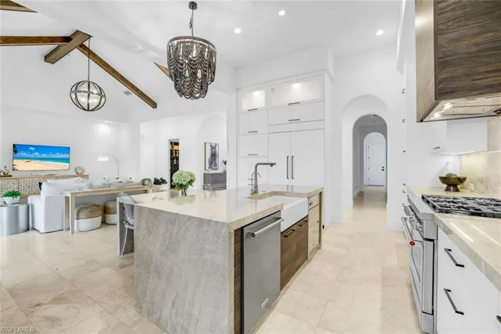 Kitchen with white cabinetry, modern cabinets, appliances with stainless steel finishes, light stone countertops, and beamed ceiling