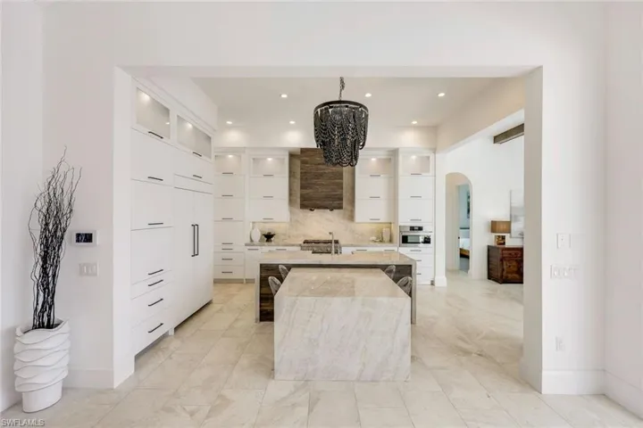 Kitchen featuring modern cabinets, arched walkways, light marble finish floors, an island with sink, and recessed lighting