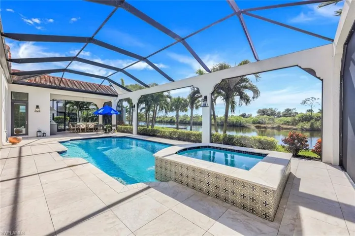 View of pool with a patio, a water view, glass enclosure, and a pool with connected hot tub