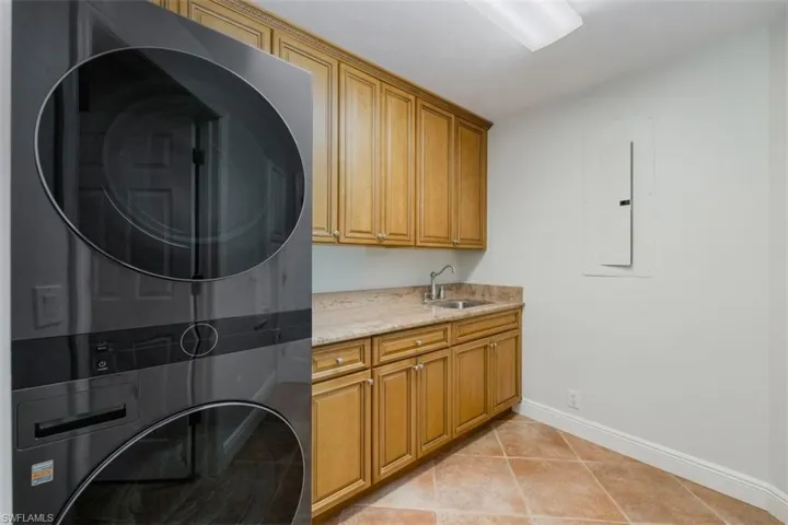 Washroom with cabinet space, light tile patterned flooring, stacked washer / drying machine, and electric panel