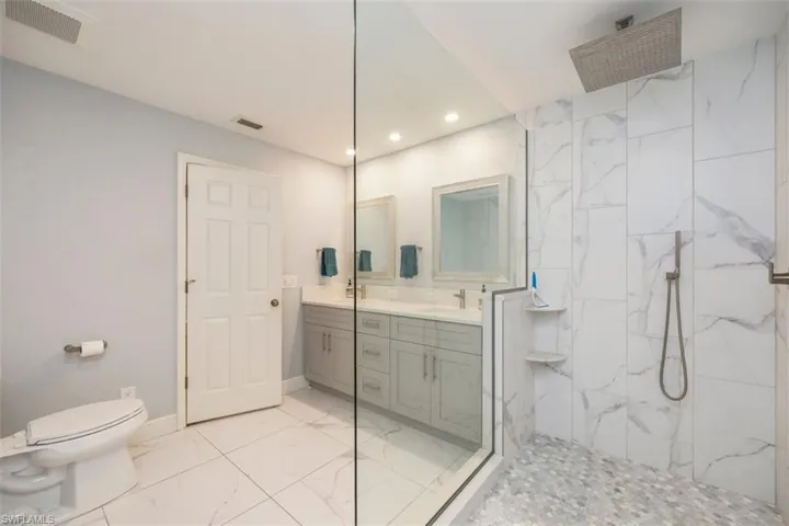 Guest Bathroom featuring light marble finish flooring, double vanity, a marble finish shower, and recessed lighting