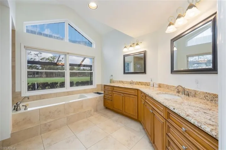 Master Bathroom featuring a bath, double vanity, vaulted ceiling, light tile patterned floors, and recessed lighting