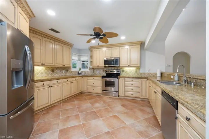 Kitchen with stainless steel appliances, decorative backsplash, light tile patterned floors, ceiling fan, and light stone countertops