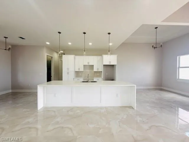 Kitchen with light stone counters, white cabinets, a large island with sink, and pendant lighting