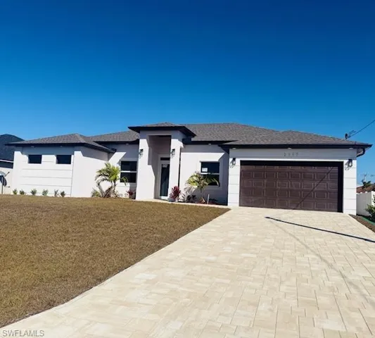Prairie-style home with an attached garage, a front lawn, decorative driveway, stucco siding, and roof with shingles