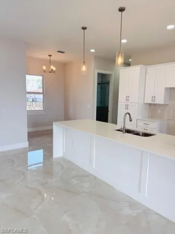 Kitchen featuring a spacious island, white cabinetry, light stone countertops, backsplash, and hanging lights