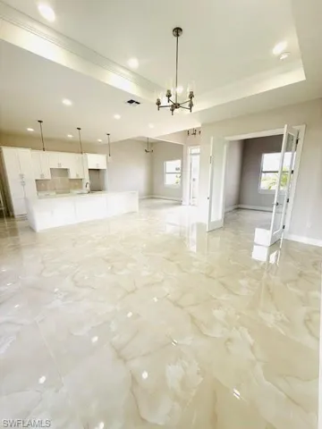 Kitchen with a center island with sink, white cabinetry, light stone counters, open floor plan, and a tray ceiling