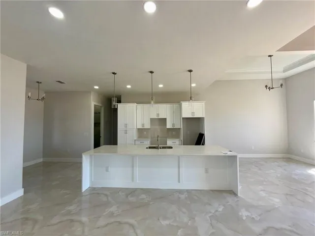 Kitchen with white cabinets, pendant lighting, light stone counters, light marble finish floors, and a center island with sink