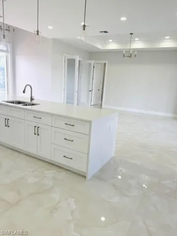 Kitchen with a center island with sink, white cabinetry, light stone counters, open floor plan, and a tray ceiling