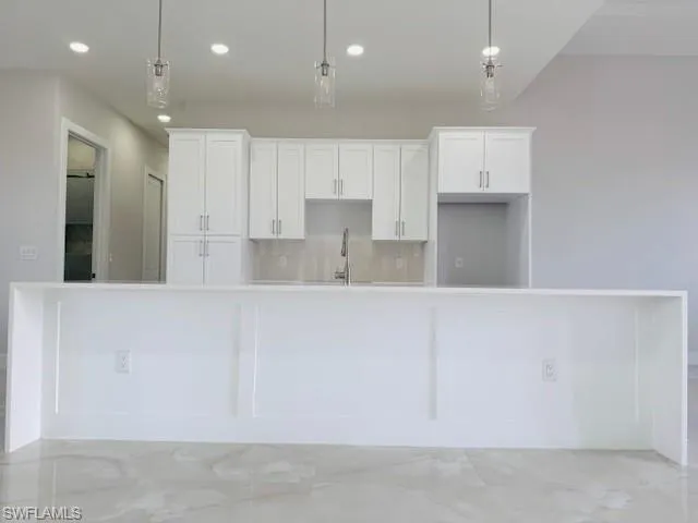 Kitchen featuring light stone countertops, white cabinets, decorative backsplash, light marble finish flooring, and suspended lighting