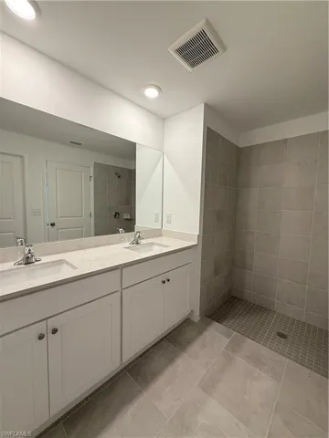 Bathroom with tiled shower, double vanity, and recessed lighting