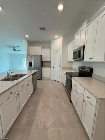 Kitchen with stove, white cabinets, light stone countertops, recessed lighting, and dishwasher