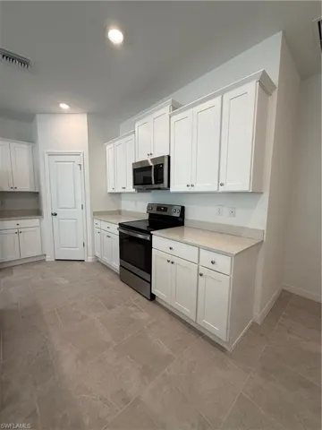 Kitchen with stainless steel range, white cabinets, light stone countertops, and recessed lighting