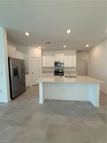 Kitchen with appliances with stainless steel finishes, white cabinetry, recessed lighting, an island with sink, and light stone countertops