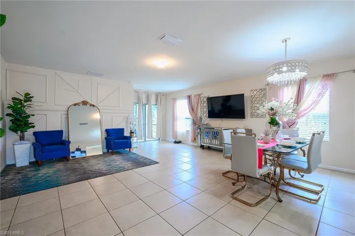 Open concept living and dining area featuring light-toned tile flooring, decorative wall paneling, and a contemporary chandelier