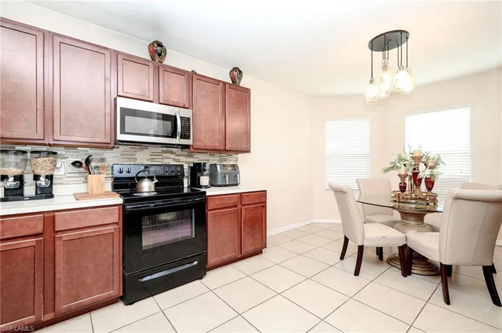 Kitchen featuring wood-finish cabinetry, stainless steel microwave, black electric range, and a mosaic tile backsplash