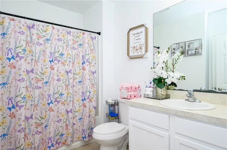 Bathroom featuring a white vanity with panel cabinetry, a light-colored countertop, and an integrated sink with a chrome faucet