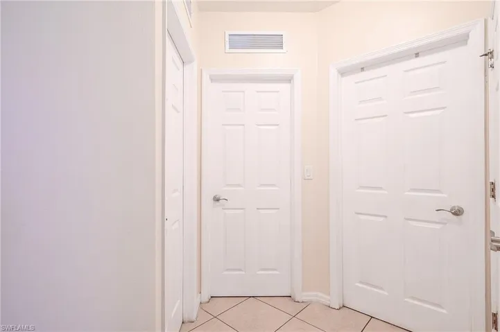 Entryway featuring light-toned tile flooring, white paneled doors with brushed nickel hardware, and a ceiling-mounted ventilation grate