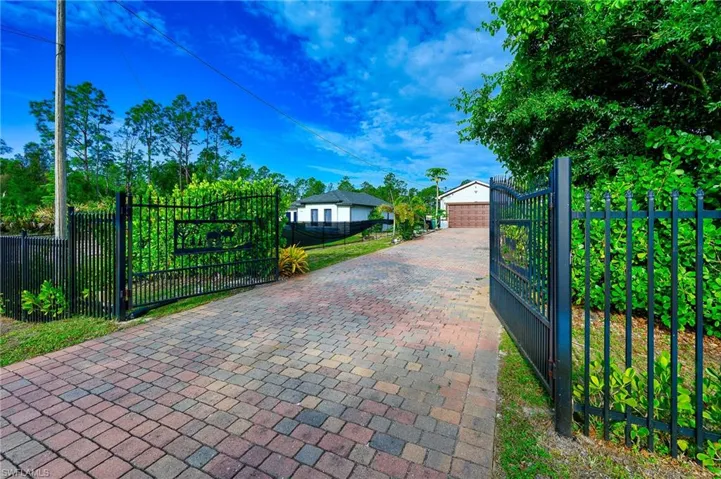 Gated entry with a multi-toned paver driveway, leading to a property featuring a white and dark-accented residence with a two-car garage