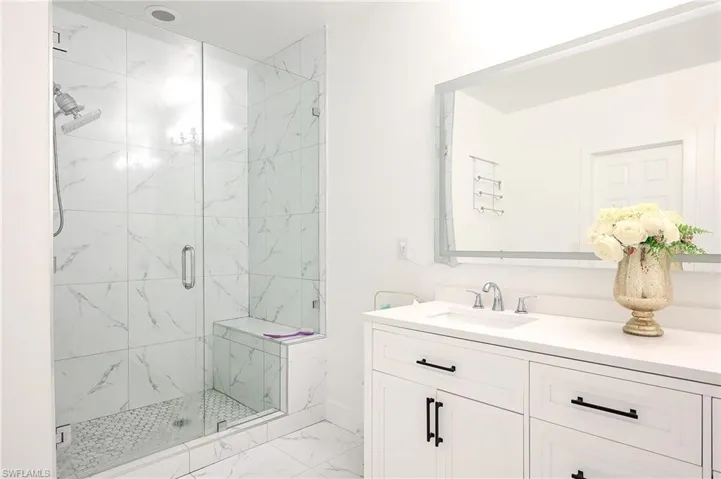 Spacious bathroom featuring a glass-enclosed shower with a built-in bench, marble-patterned tile, and a hex-tile shower floor