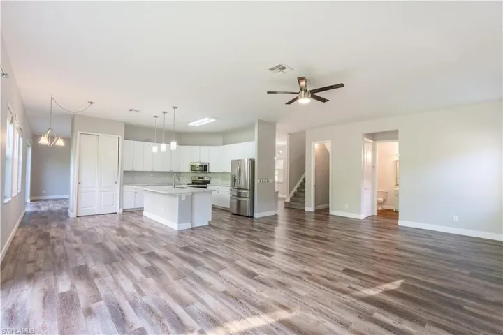 Unfurnished living room with dark wood-style flooring, stairs, ceiling fan, and a chandelier