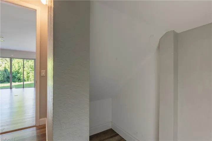 Storage room with a textured wall and dark wood finished floors beneath stairs.
