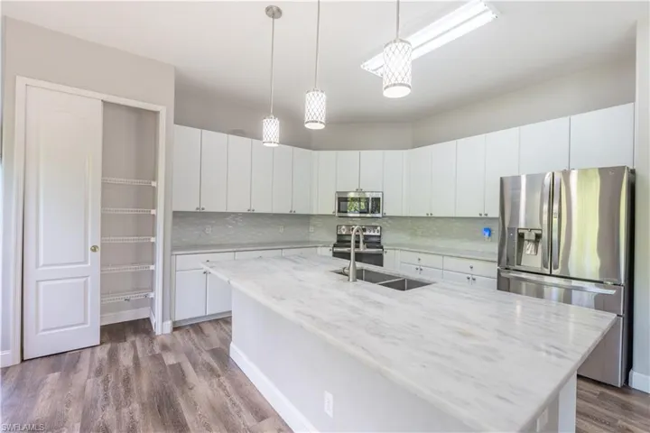 Kitchen with stainless steel appliances, hanging light fixtures, white cabinetry, a kitchen island with sink, and light stone countertops