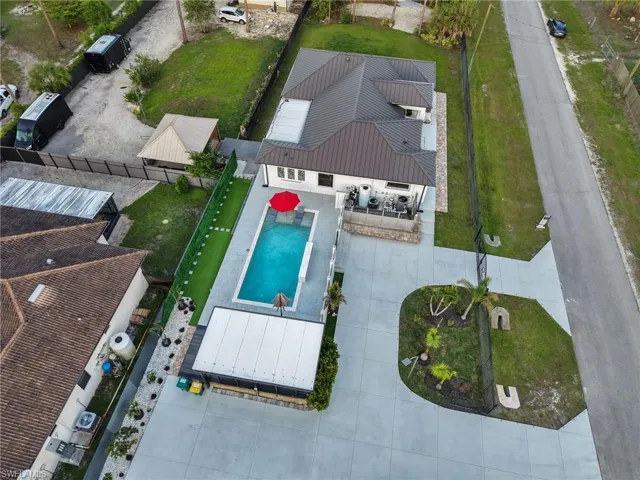 Contemporary residence featuring a rectangular pool with surrounding patio, a concrete driveway, a dedicated covered patio area, and a secondary structure with a gabled roof