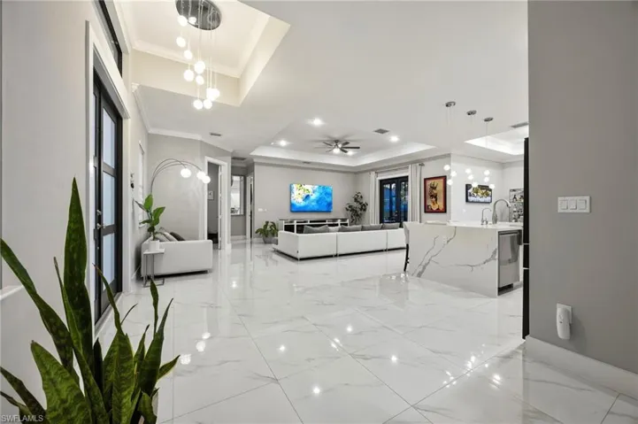 Spacious interior featuring large format marble-look tile flooring, a contemporary kitchen island with a waterfall countertop, and a tray ceiling with recessed lighting