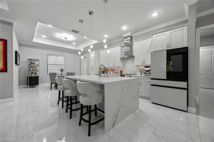 Gourmet kitchen featuring a waterfall island with integrated seating, white shaker cabinetry, stainless steel appliances, and a tray ceiling with recessed lighting