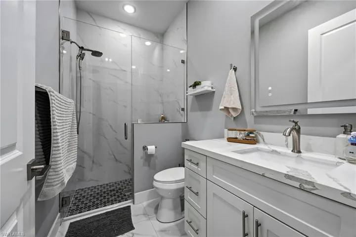 Modern bathroom featuring a glass-enclosed shower with white marble-patterned wall tiling and black mosaic floor tiling