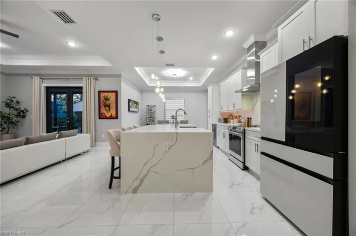 Contemporary kitchen featuring a waterfall-edge island, white shaker-style cabinetry, stainless steel appliances, and large format tile flooring