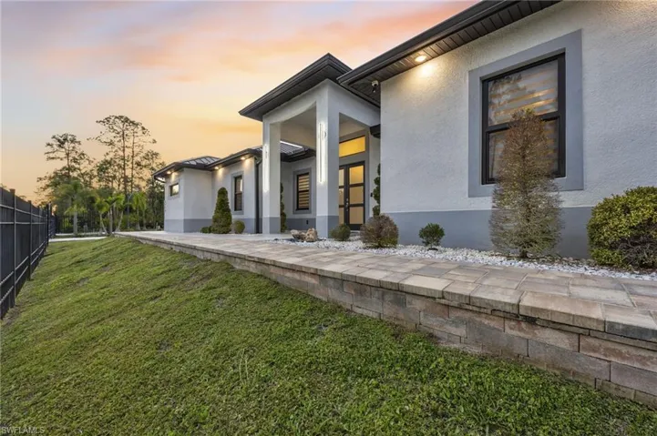 Contemporary exterior featuring a stucco finish, dark framed windows, and a paved walkway with a stone retaining wall