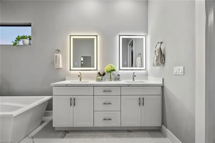 Dual vanity in primary bathroom with white cabinetry, integrated sinks, and polished chrome fixtures