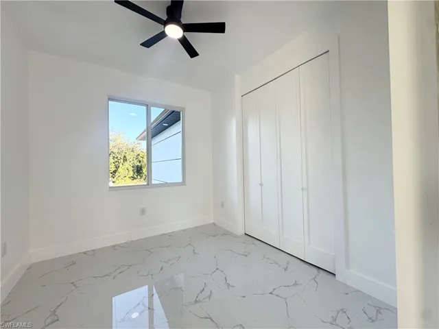 Unfurnished bedroom featuring light marble finish floors, ceiling fan, and a closet