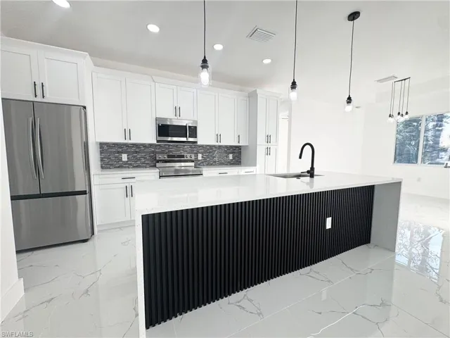 Kitchen with appliances with stainless steel finishes, light stone countertops, a spacious island, hanging light fixtures, and recessed lighting