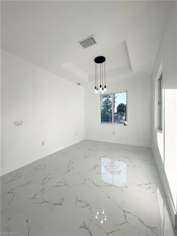 Empty room featuring a tray ceiling and light marble finish floors
